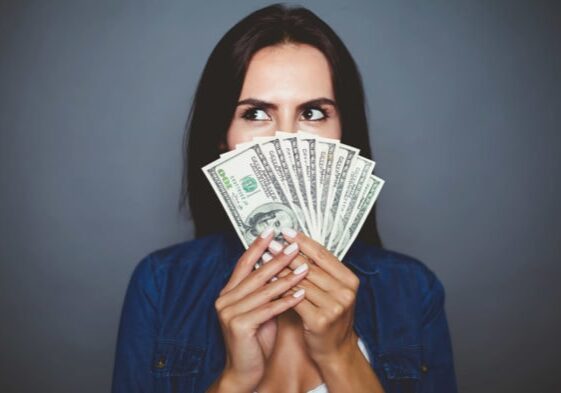You can make purchases. Beautiful young woman in casual clothes joyfully holding in her hand a lot of dollars on a gray background isolated. The concept of money and banking.